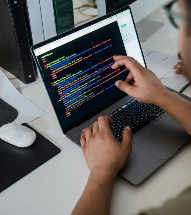 Close-up of a programmer pointing at a colorful code script on a laptop in an office setting.